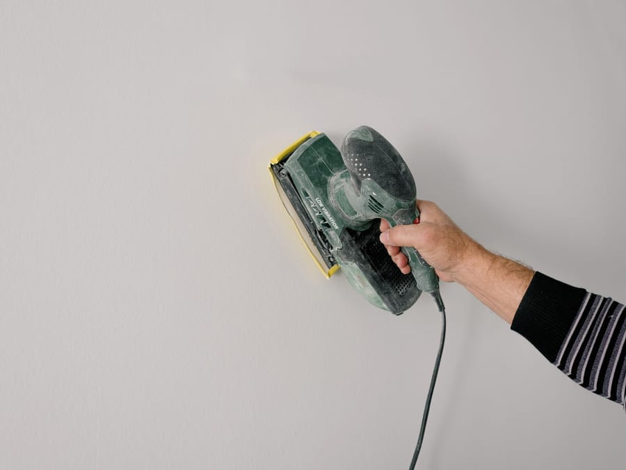 A wall being sanded smooth by hand, the surface readied before any finish is opened.