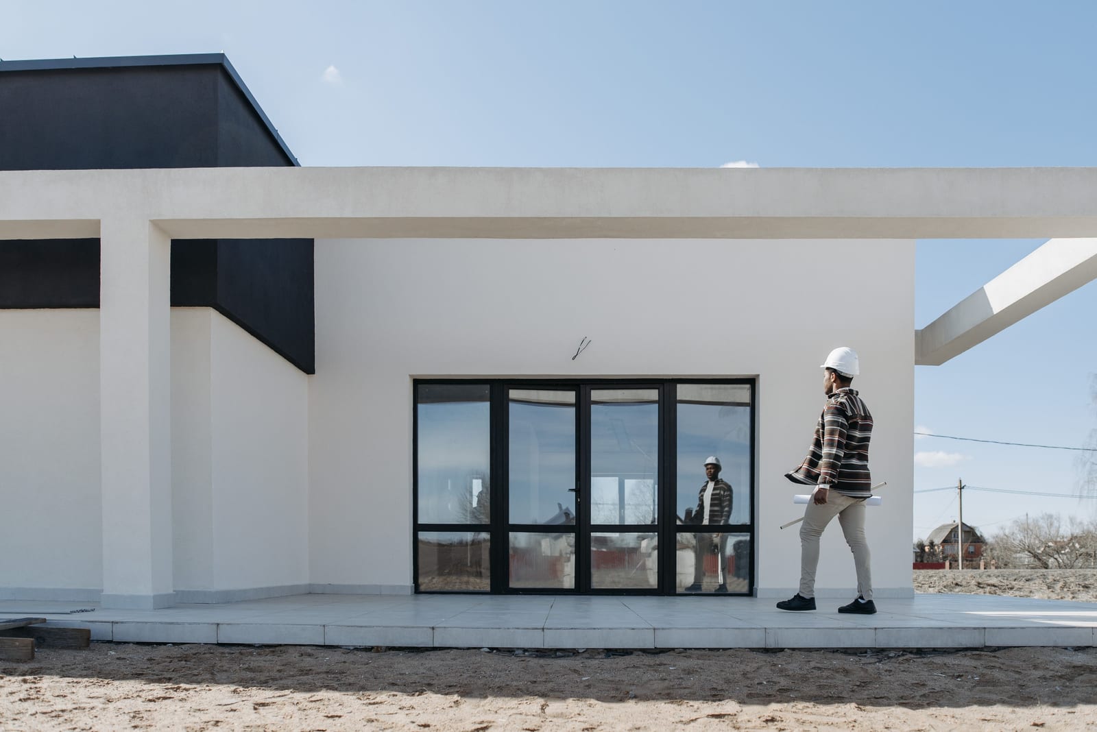 A figure crossing the terrace of a newly completed building, drawings in hand and the finished elevation behind.