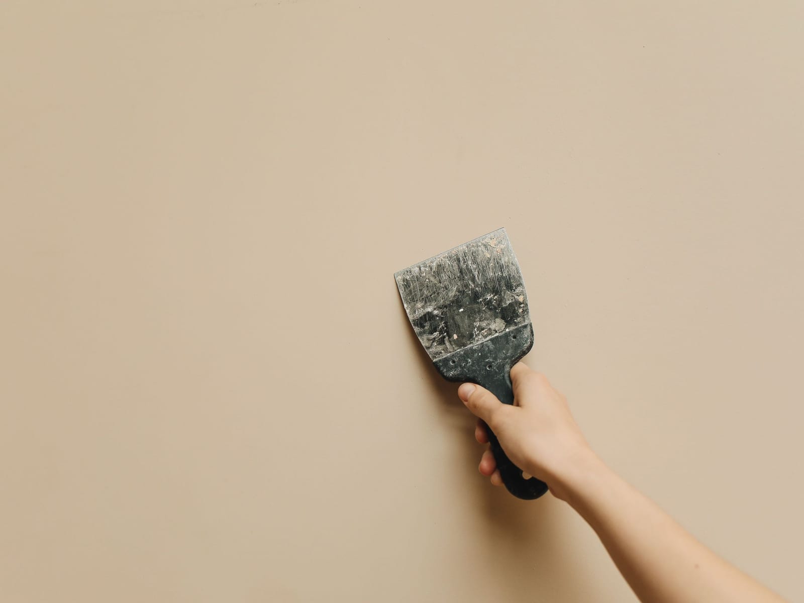 A taping knife drawing compound across a wall, the repair feathered out and left to be sanded.