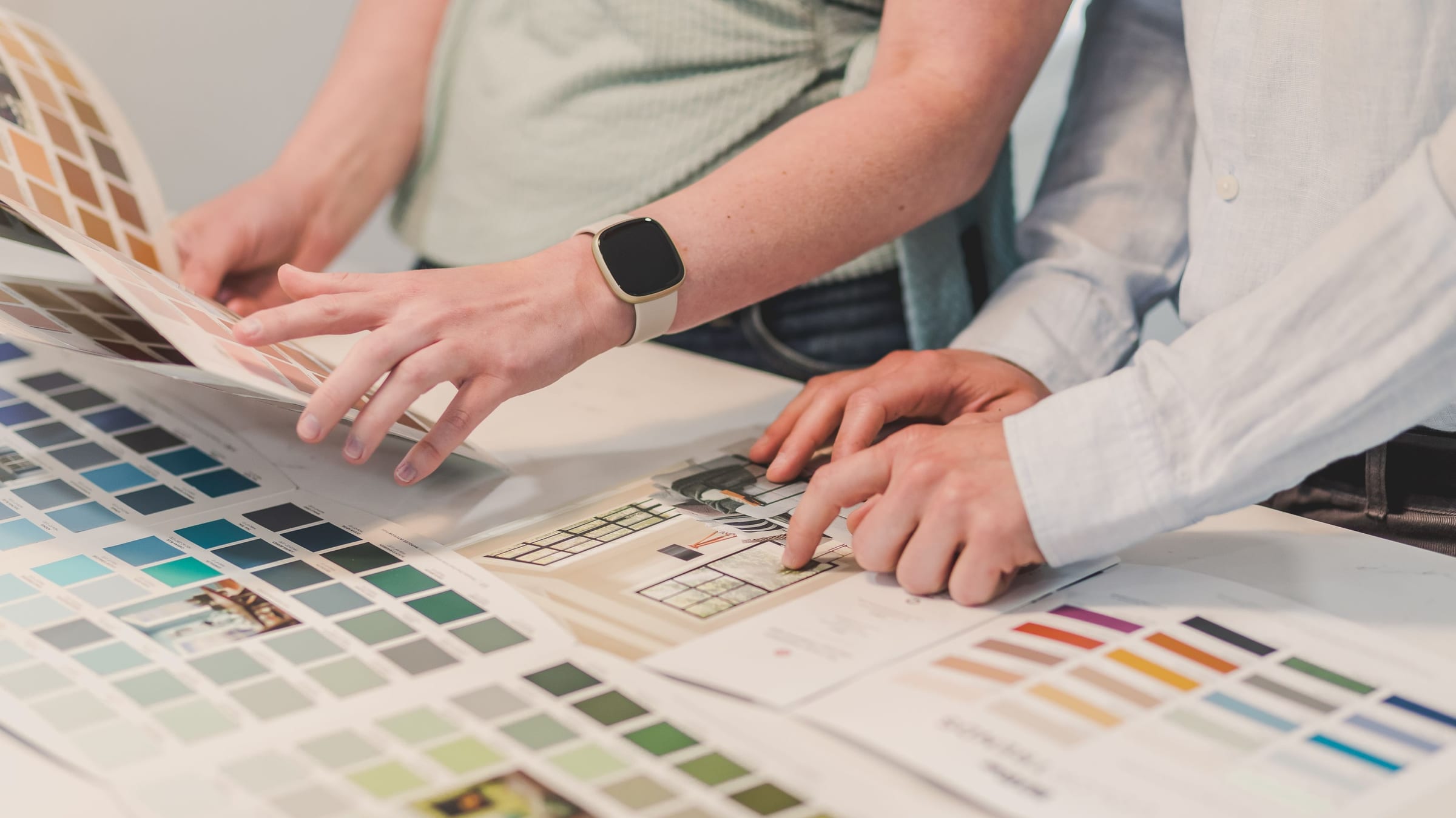 Two people leaning over a table of colour charts and drawings, mid-conversation, choosing between finishes together.