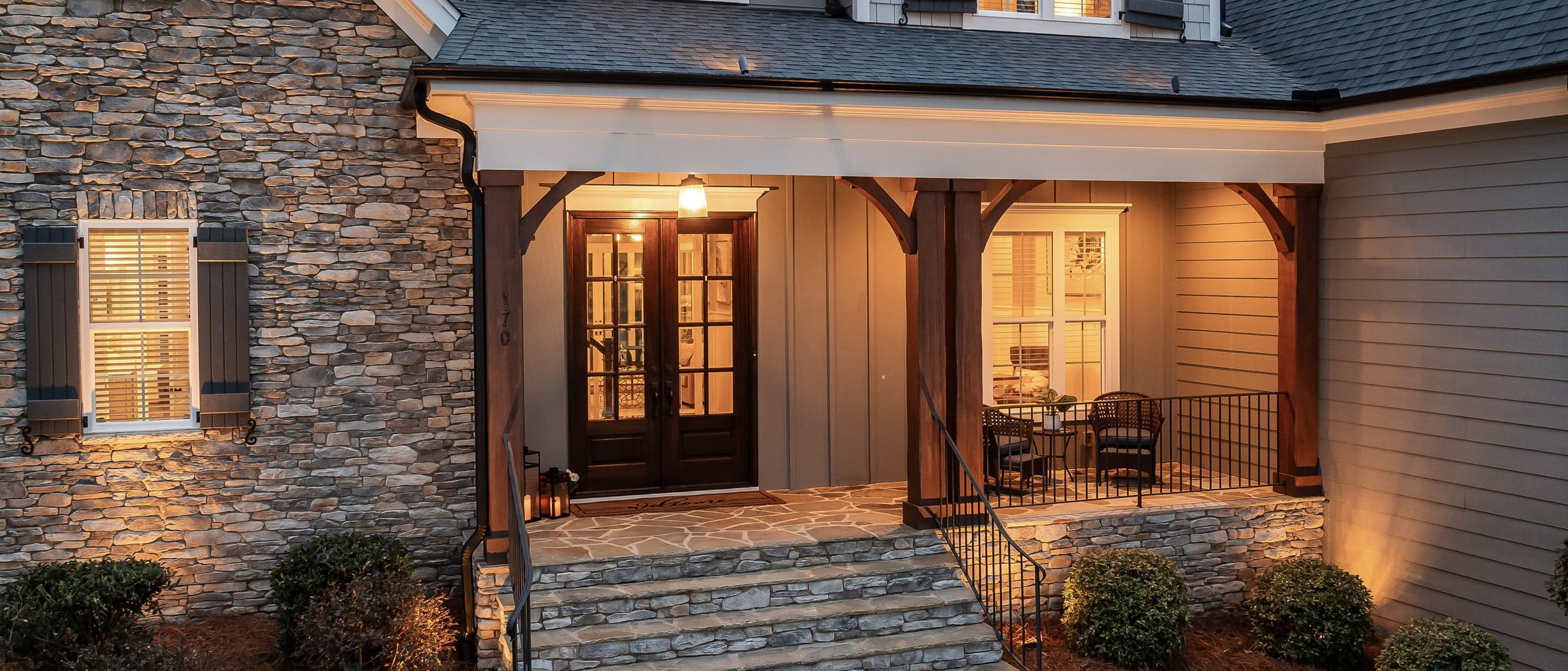 An Alaska residence at dusk, warm light spilling from the windows and doorway across a covered porch.