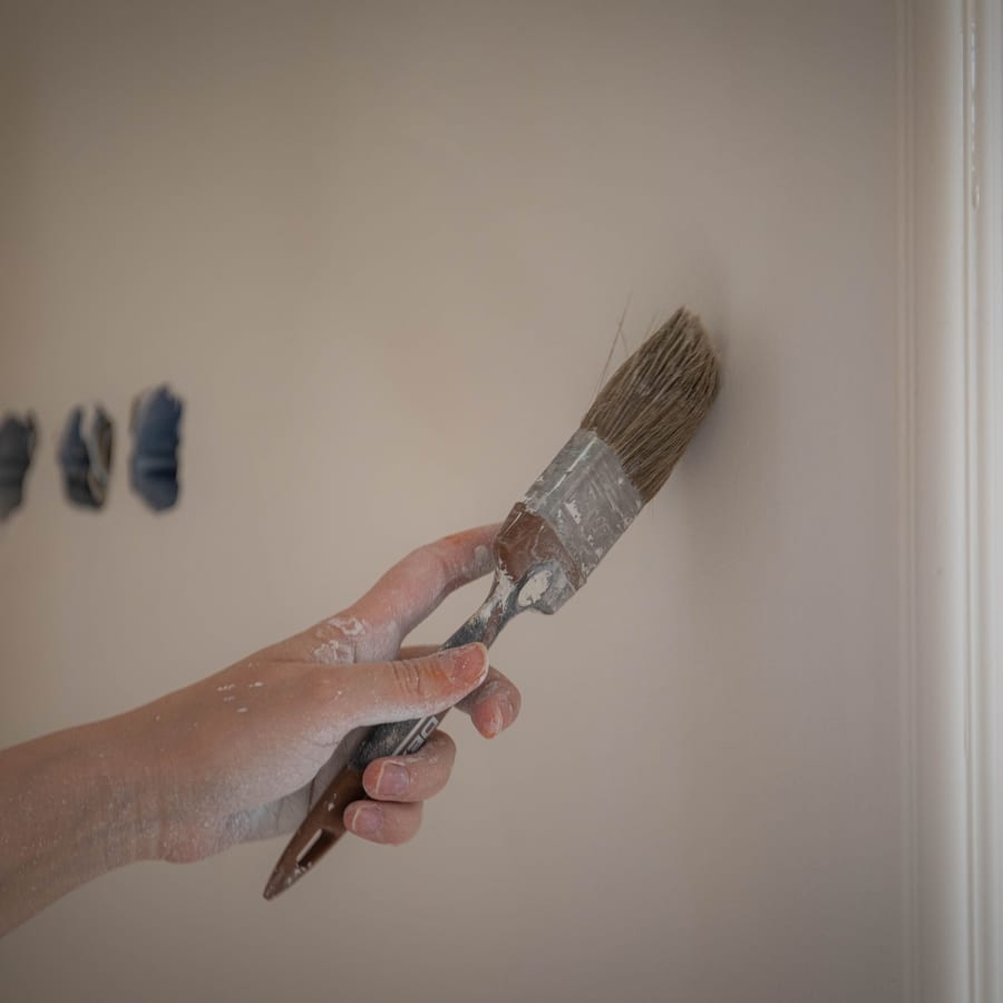 A hand drawing a loaded brush along a wall, the stroke held steady and even.