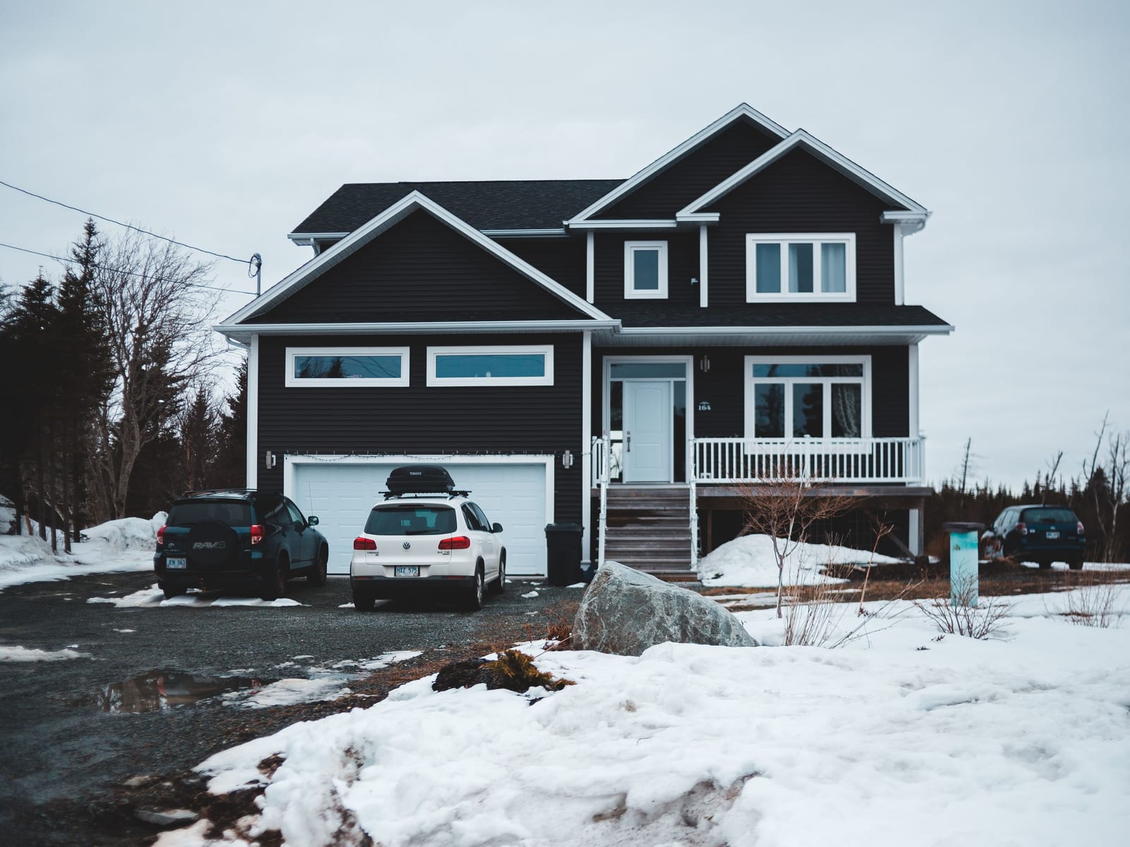 A dark-bodied home with white trim under snow, the contrast between siding and casing doing all the work.