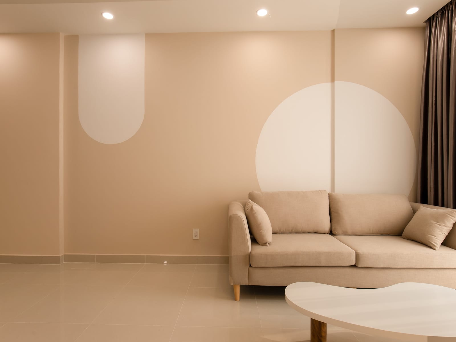 A quiet room in warm neutral tones, a curved painted form on the wall catching soft afternoon light.