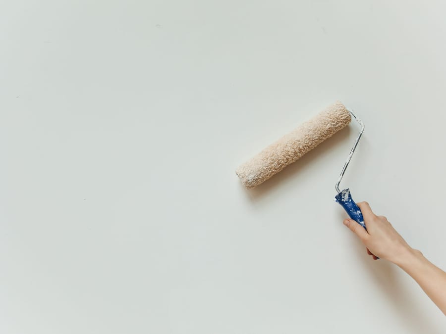 A roller drawing an even coat of paint across a prepared wall.