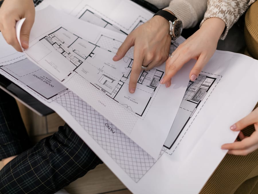 Two people tracing a floor plan together, hands over the drawing as the work is discussed.