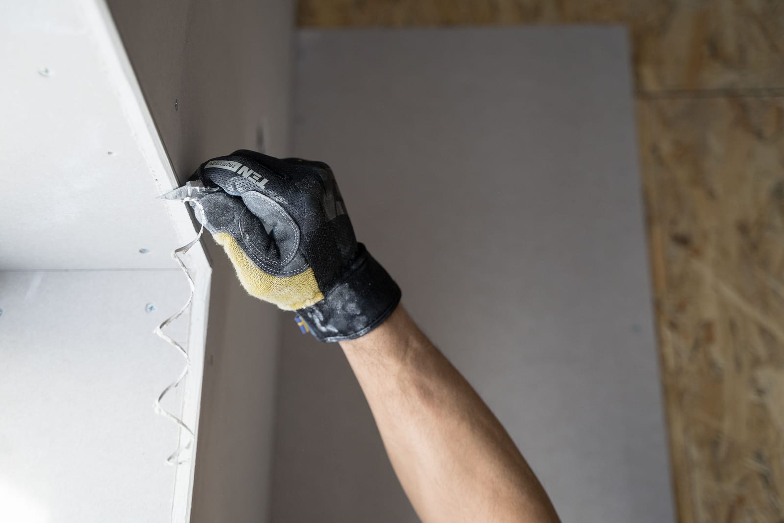 A drywall knife drawing compound across a seam, the surface feathered smooth in raking light.