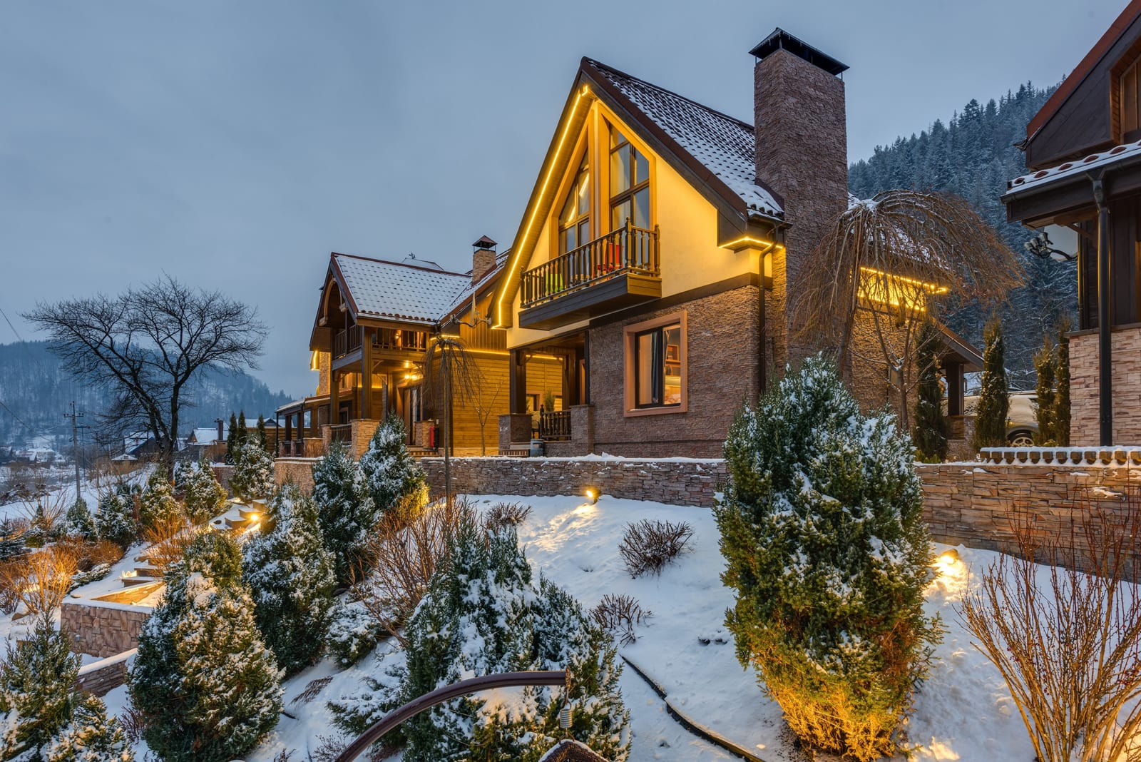 A timber and stone mountain residence with freshly finished siding and trim, snow banked to the windows beneath an evening sky.