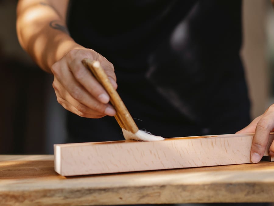 Stain being drawn along a timber board, the colour deepening evenly behind the brush.
